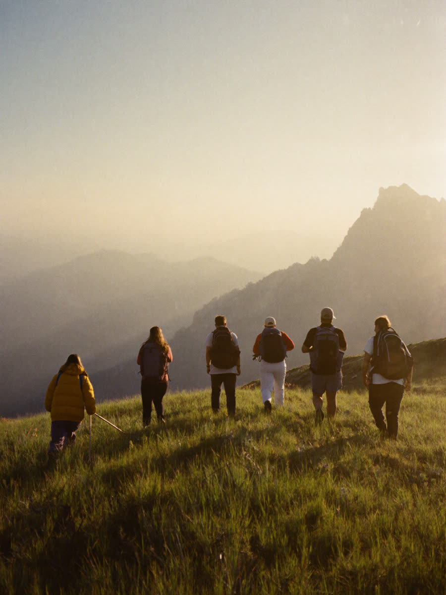 Hikers cresting a grassy ridge toward a sunlit peak at dawn
